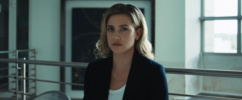 Lili Reinhart com expressão séria usando blazer preto em cena do filme Rede Tóxica da HBO Max.