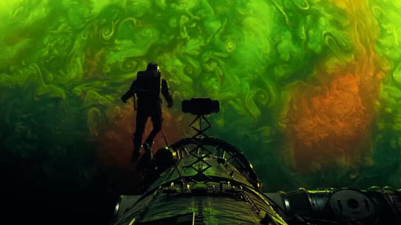 Astronauta Ryland Grace flutuando do lado de fora da nave Hail Mary em direção a uma nebulosa de cores verdes e laranjas intensas no filme Devoradores de Estrelas.