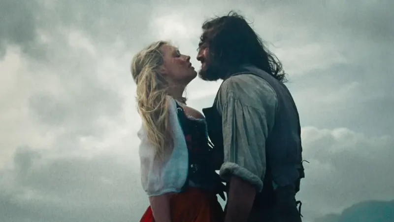 Cena de O Morro dos Ventos Uivantes 2026 com Margot Robbie e Jacob Elordi abraçados sob céu nublado.