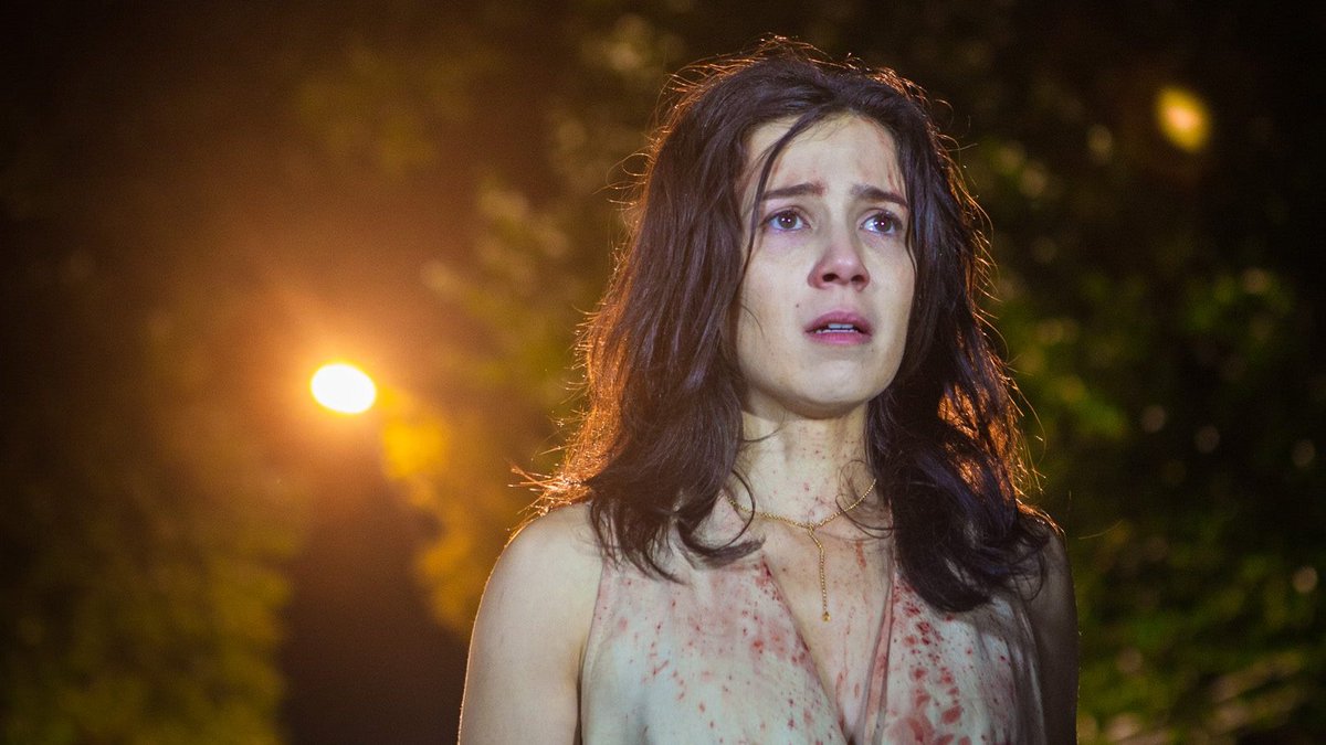 Marjorie Estiano com expressão de choro, desespero e lágrima nos olhos, vestindo um vestido claro manchado de sangue em uma rua escura à noite, ilustrando as novidades nos streamings.
