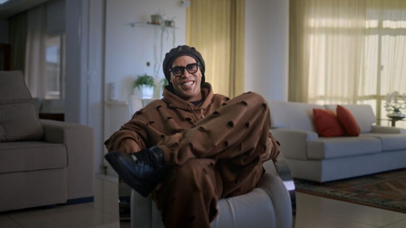 Ronaldinho Gaúcho sorridente, usando boina e óculos, em uma cena do documentário da Netflix que está entre os melhores filmes e séries de abril.