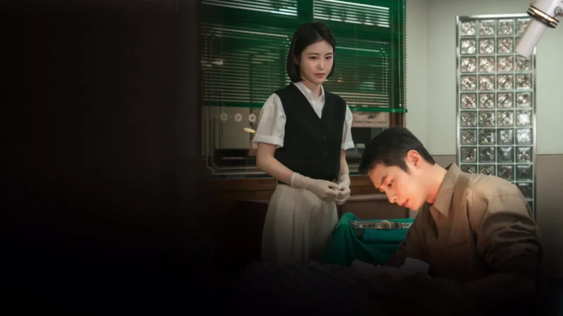 A atriz Shin Ye-eun caracterizada como enfermeira observa o ator Lee Jae-wook de gola médica em um consultório de hospital, ilustrando as novidades nos streamings.