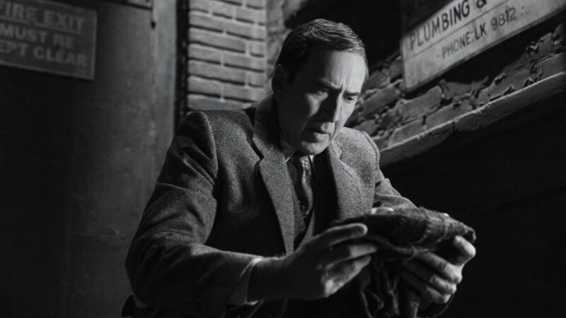 O que assistir nos streamings: o ator Nicolas Cage em cena preto e branco da série Spider-Noir analisando um objeto misterioso.
