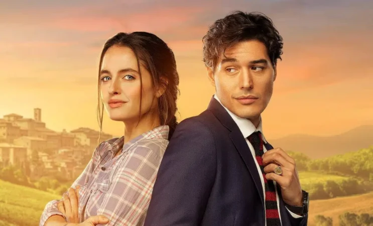 Casal protagonista do filme Da Toscana com Amor encostado de costas um para o outro com uma vila italiana ao fundo