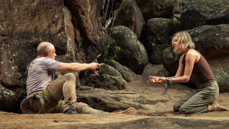 Charlize Theron ajoelhada e acorrentada em uma cena de sobrevivência no filme O Jogo do Predador, um dos destaques de os melhores filmes e séries de abril na Netflix.