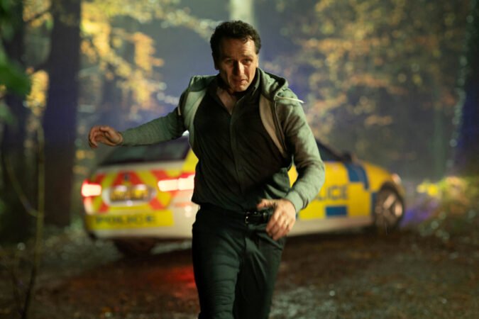 Matthew Rhys correndo de uma viatura policial em cena de Hallow Road: Caminho Sem Volta.