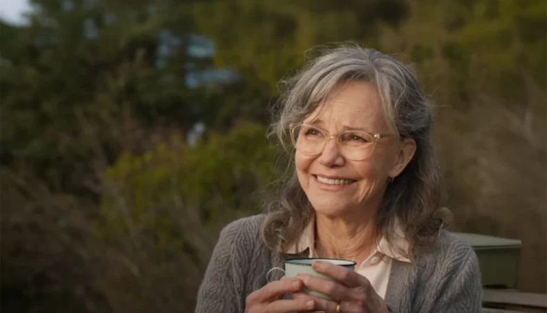 A atriz Sally Field sorrindo afetuosamente enquanto segura uma caneca, ilustrando a jornada emocional e o significado de Criaturas Extraordinariamente Brilhantes.