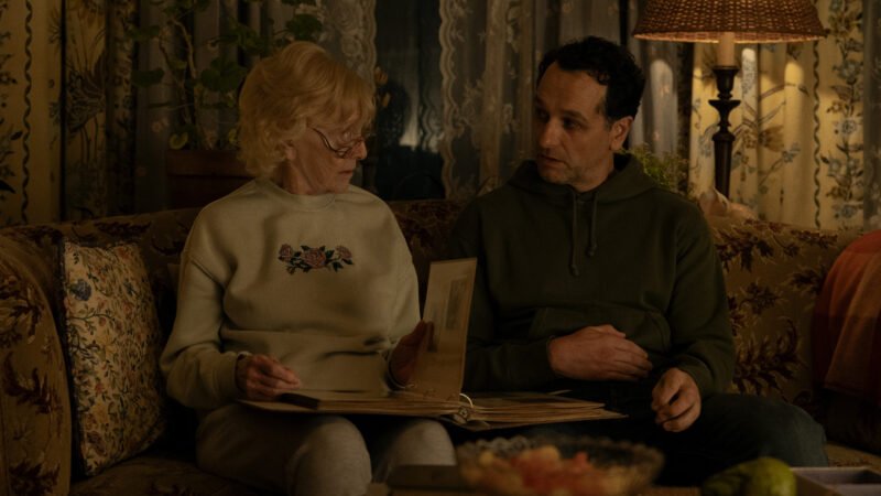 Matthew Rhys em cena no sofá investigando documentos e pistas em O Segredo de Widow's Bay.