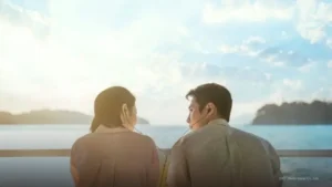 O ator Lee Jae-wook e a atriz Shin Ye-eun vistos de costas e de perfil, dividindo o mesmo fone de ouvido enquanto se encaram em um barco durante o pôr do sol, ilustrando quantos episódios tem Doutor à Beira do Amor.