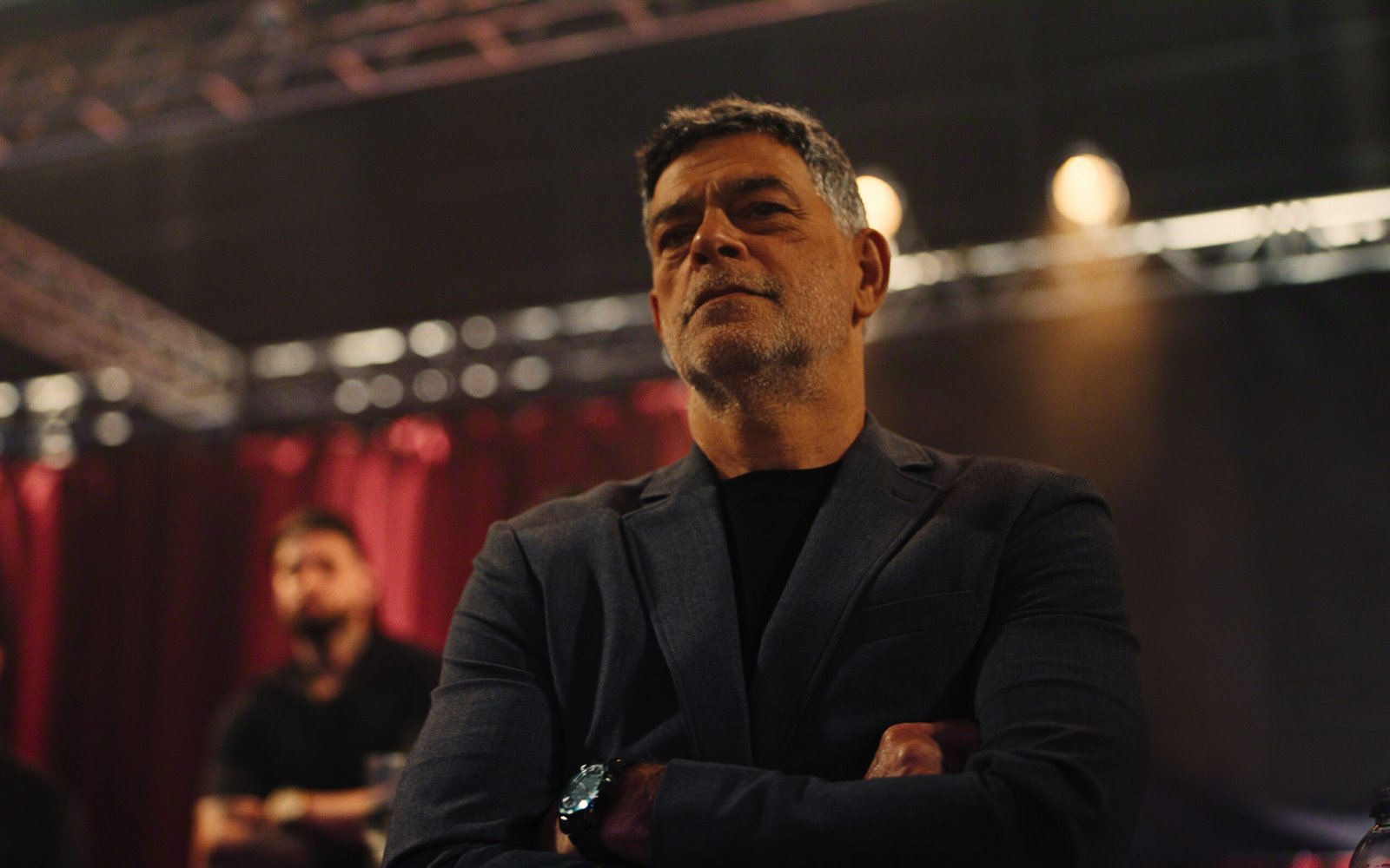 Eduardo Moscovis de braços cruzados na arena de MMA em cena que marca a estreia dos streamings de julho.