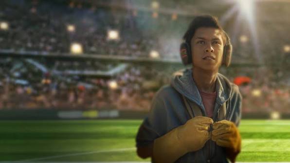 Jovem de luvas e abafador no gramado em cena do filme Um Goleiro Muito Improvável para o guia de o que assistir nos streamings em julho.