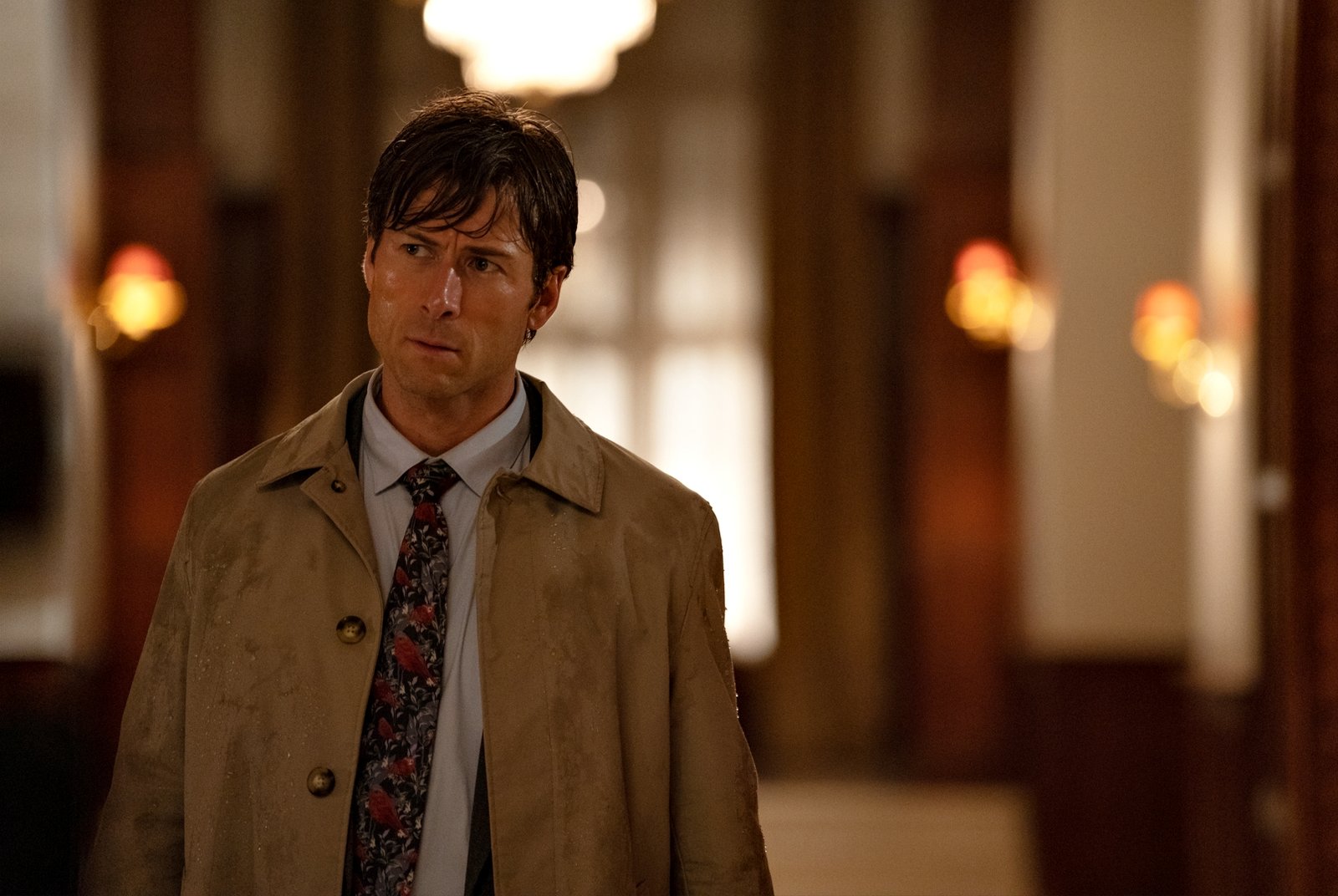 Glen Powell de sobretudo bege em cena de mistério para o guia de estreias do streaming.