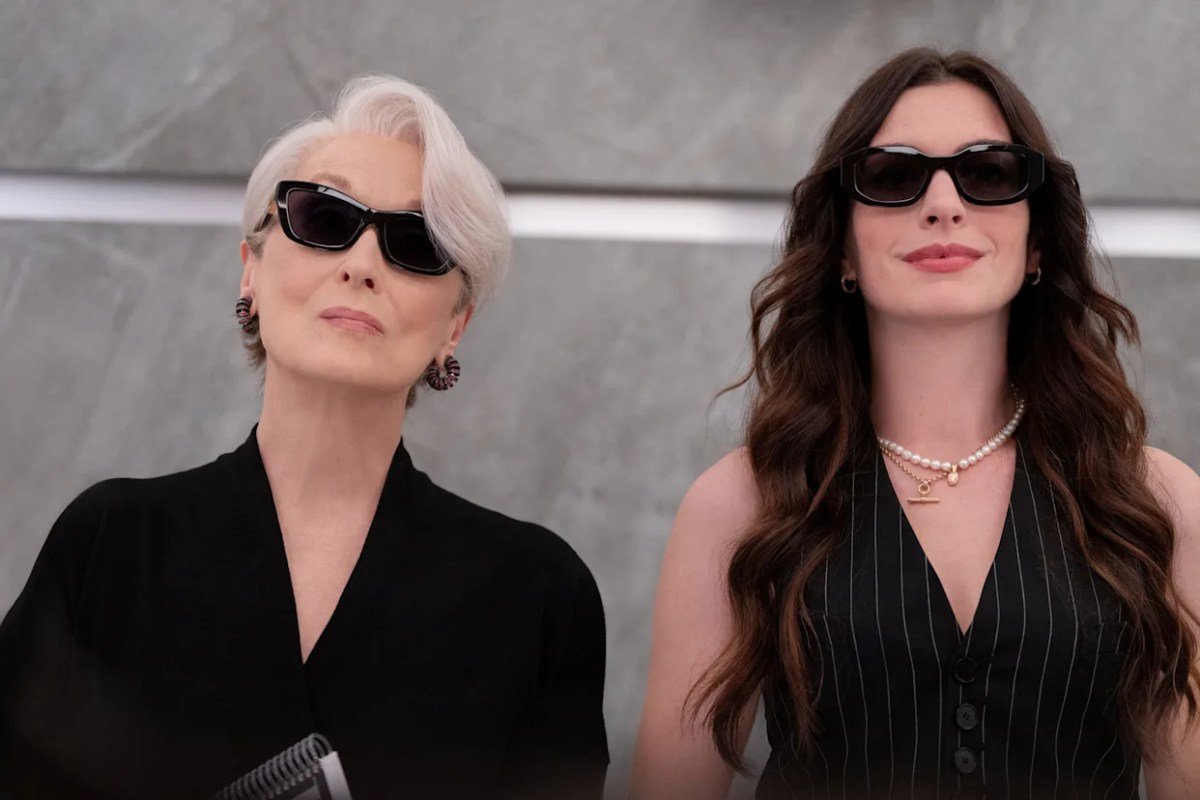 As atrizes Meryl Streep e Anne Hathaway, lado a lado vestindo roupas pretas elegantes e óculos de sol escuros, olham para a frente com expressão confiante e poderosa nas estreias dos streamings de julho.