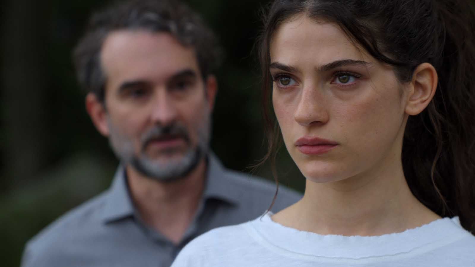 Close da atriz Ella Rubin com expressão séria em primeiro plano e um homem desfocado ao fundo na série Sterling Point, grande destaque entre as estreias de agosto no streaming.