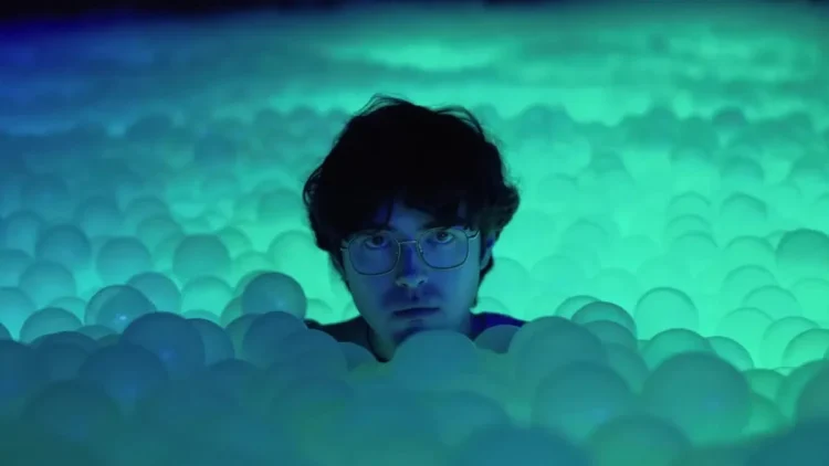 O ator James Sweeney imerso em uma piscina de bolinhas com iluminação verde no filme Twinless.