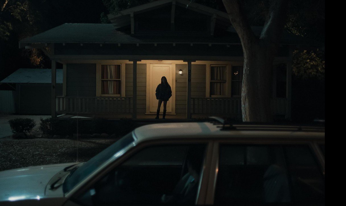 Silhueta de mulher na varanda iluminada em cena de suspense do filme Obsessão.