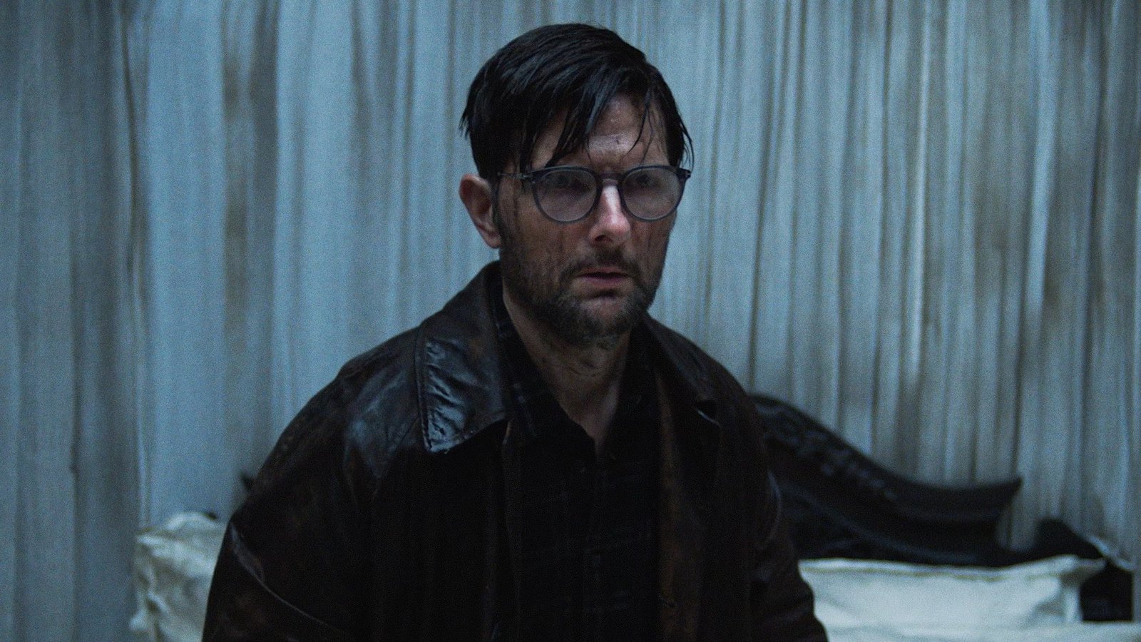Adam Scott com expressão de pânico e óculos embaçados em cena de Hokum – O Pesadelo da Bruxa, destaque de terror na lista de filmes e séries de agosto.