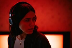 Mulher com fones de ouvido olhando para o lado em uma sala com iluminação vermelha tensa no filme Undertone.