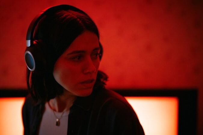 Mulher com fones de ouvido olhando para o lado em uma sala com iluminação vermelha tensa no filme Undertone.