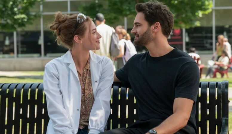 Lili Reinhart e Tom Bateman como Olive e Adam, sorrindo em um banco no filme A Hipótese do Amor (2026).