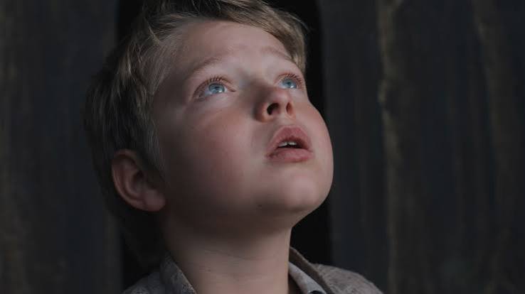 Jacobi Jupe como Hamnet, olhando para cima com expressão apreensiva, destaque entre crianças em filmes e séries.