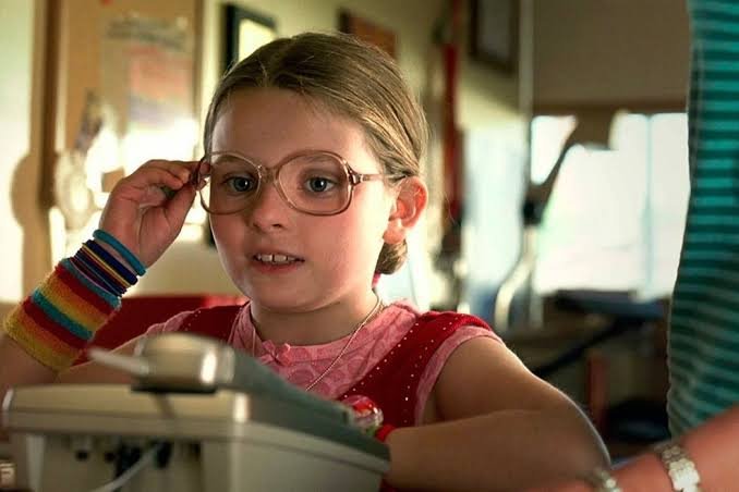 Abigail Breslin como Olive Hoover ajustando seus óculos em Pequena Miss Sunshine, destaque entre crianças em filmes e séries.