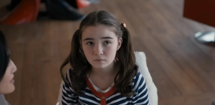 Shannon Mahina Gorman como Mia Kawasaki, sentada à mesa em Família de Aluguel, destaque entre crianças em filmes e séries.