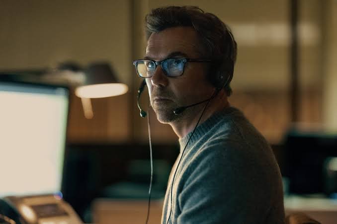 Patrick Brammall como Ian Ridley usando headset diante de um computador em Desaparecida 2026.