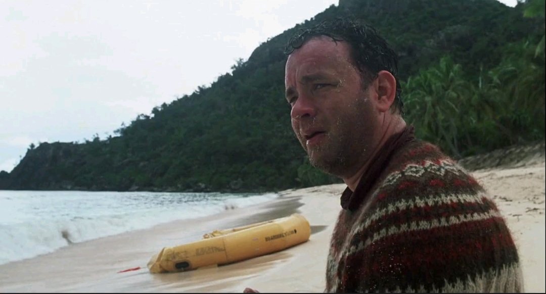 Tom Hanks como Chuck Noland em uma praia deserta diante do oceano em Náufrago, um dos filmes sobre o mar.