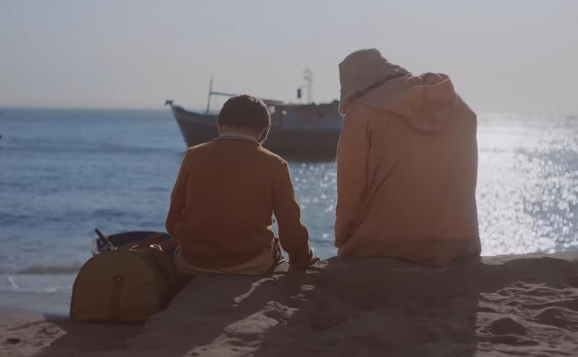 Homem e menino sentados à beira-mar observam um barco de pesca em O Filho de Mil Homens, um dos filmes sobre o mar.