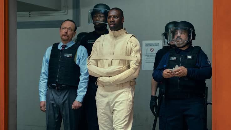Omar Sy como Assane Diop sob escolta em Lupin Parte 4, uma das novidades de outubro na Netflix.